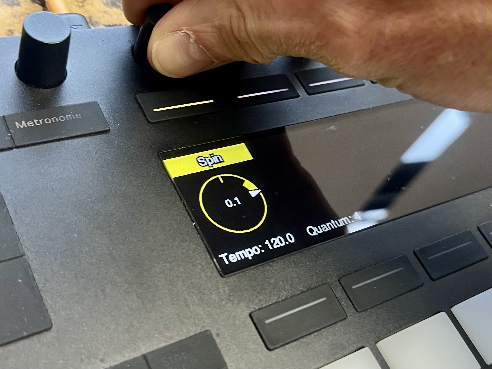 A close-up of an Ableton Push 2 with a hand touching an encoder knob and a dial shown on the screen in yellow with the label 'Spin'